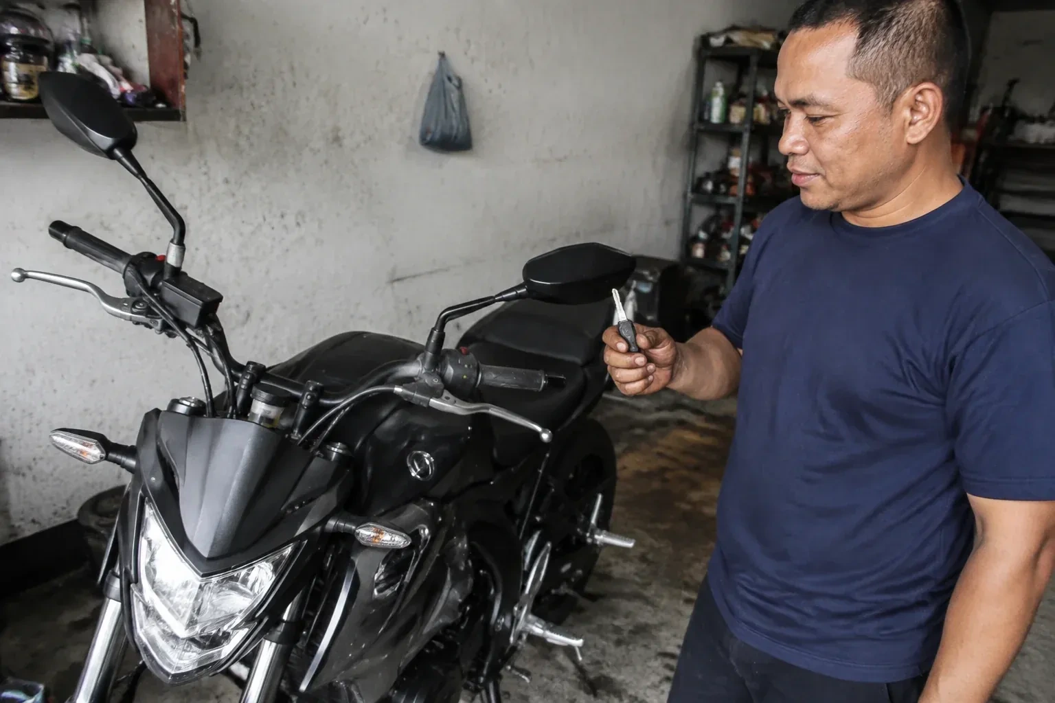 Person holding a key beside a black motorcycle in a garage. — Motorcycle & Scooter Keys, Springwater