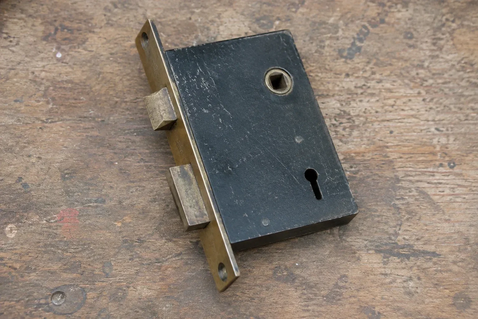 Closed mortise lock case with spindle opening, keyhole, latch and deadbolt on a wooden workbench. — Vintage Mortise Lock Service, Springwater