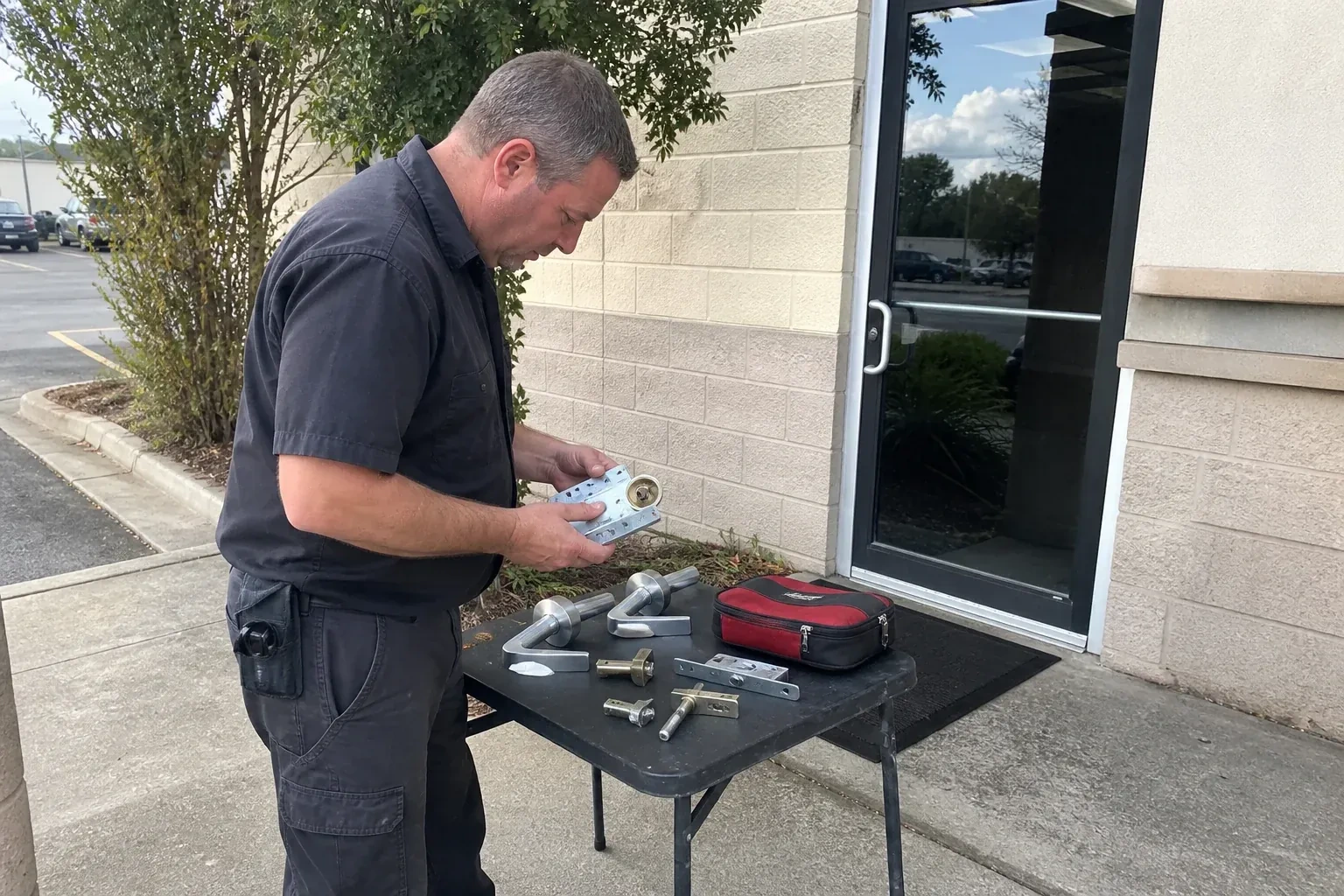 Technician examining detached commercial lock hardware on a table outside a shop entrance. — Business Lockout Service, Springwater